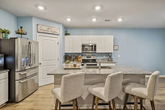 a kitchen with stainless steel appliances granite countertop a dining table chairs refrigerator and sink