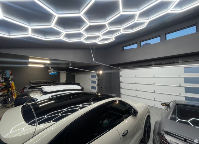 3667 Little Cottonwood Road, Unit 1 Sandy, UT 84092 - Photo 49 of 49 Garage featuring a honeycomb LED lighting system, multiple overhead windows, dark gray painted walls, and white sectional garage doors with frosted glass panels