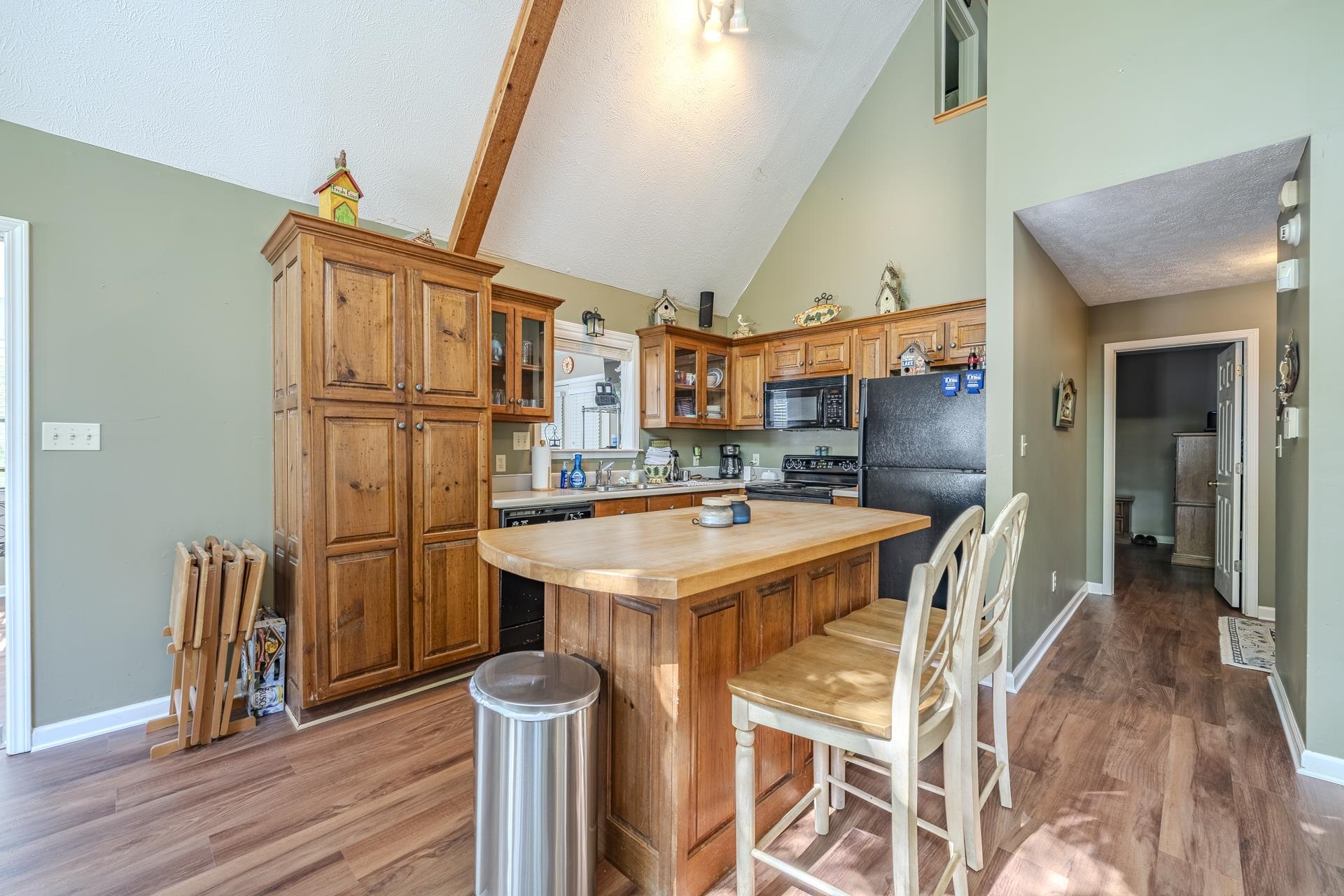 435 Murray Lane Counce, TN 38326 - Photo 14 of 34 Kitchen featuring vaulted ceilings with exposed wood beams, wood-finish flooring, a central island with bar seating, wood cabinetry, and a black appliance suite