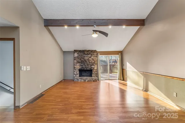 an empty room with wooden floor fireplace and windows