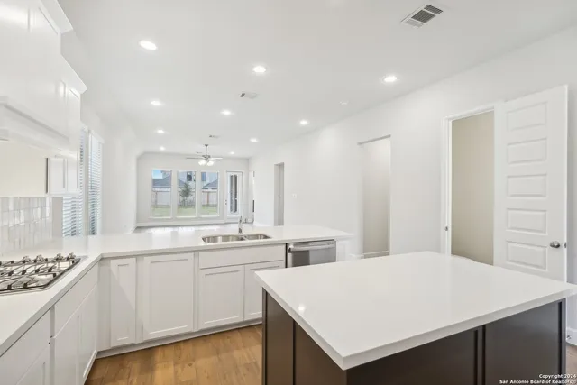 a kitchen with a sink a stove a refrigerator and white cabinets with wooden floor