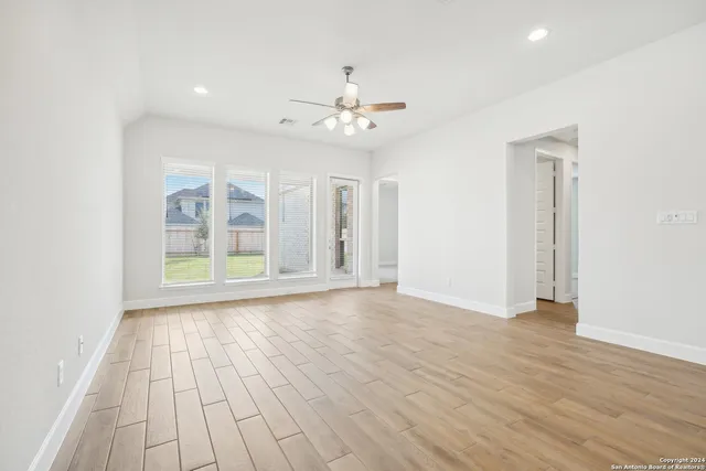 an empty room with wooden floor chandelier fan and windows