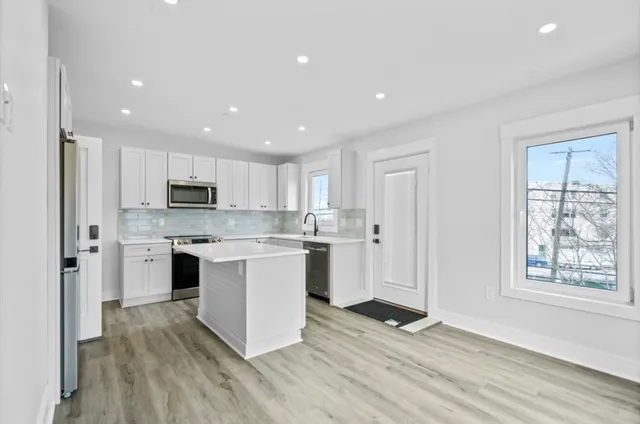 a kitchen with stainless steel appliances granite countertop a refrigerator a sink dishwasher a stove and white countertops with wooden floor