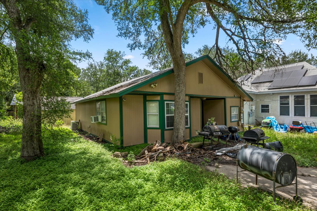 151 High Ridge Drive Del Valle, TX 78617 - Photo 6 of 8 A modest side exterior showcases lush greenery and an adjacent structure with solar panels, offering a blend of natural appeal and energy efficiency.