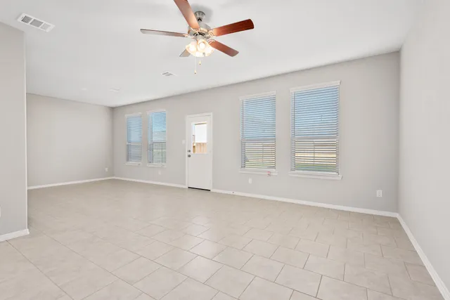 an empty room with chandelier fan and windows