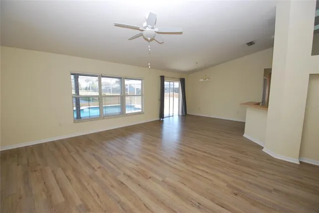 an empty room with wooden floor chandelier fan and windows