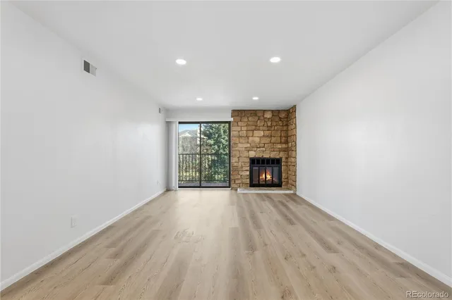 an empty room with wooden floor fireplace and windows