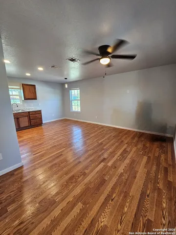 an empty room with wooden floor chandelier fan and windows