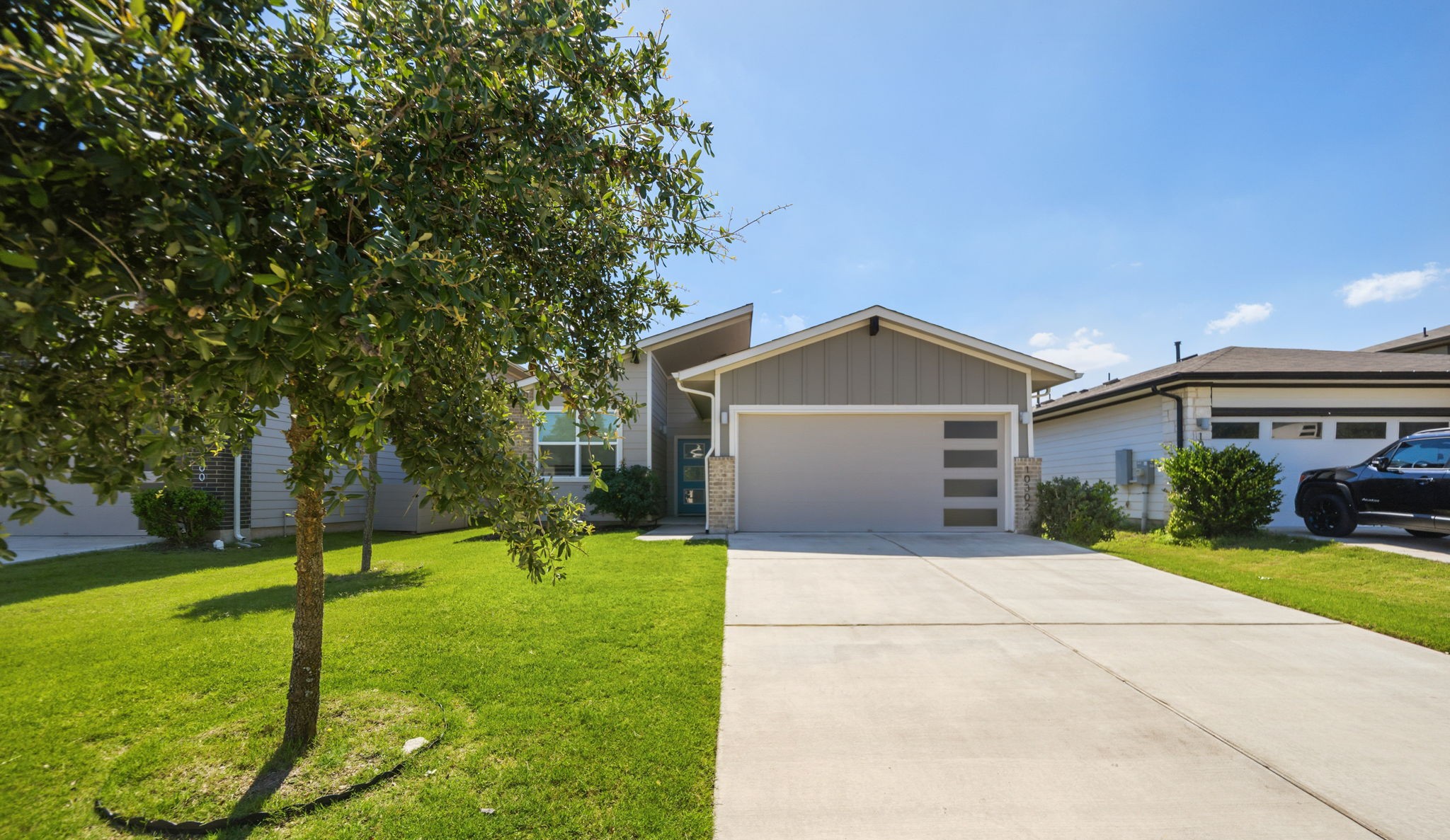 10302 Criswell Road Austin, TX 78754 - Photo 1 of 1 Modern home exterior featuring a two-car garage with frosted glass panels, an extended concrete driveway, and a manicured front lawn