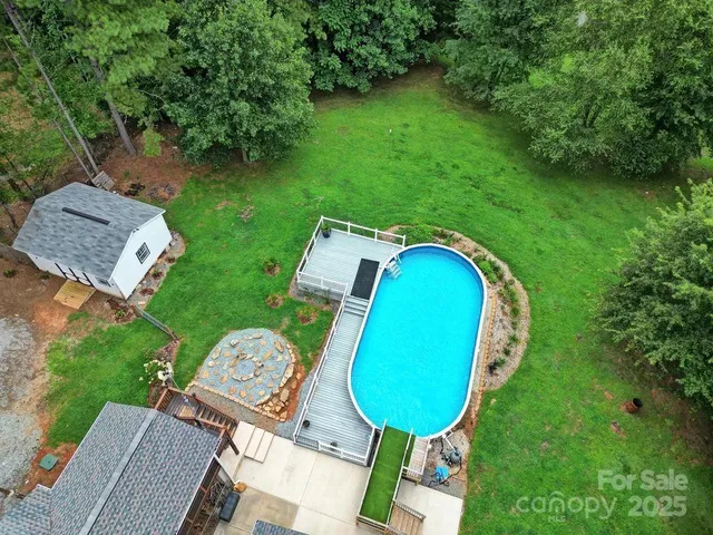 an aerial view of a house with swimming pool and trees all around