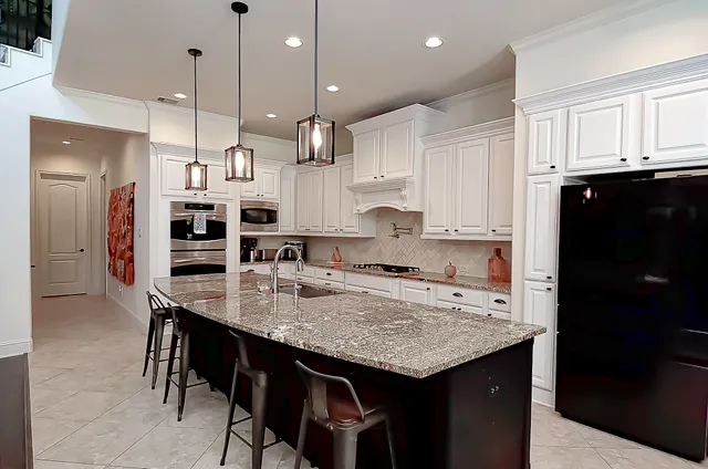 a kitchen with stainless steel appliances kitchen island granite countertop a stove a sink a refrigerator and white cabinets