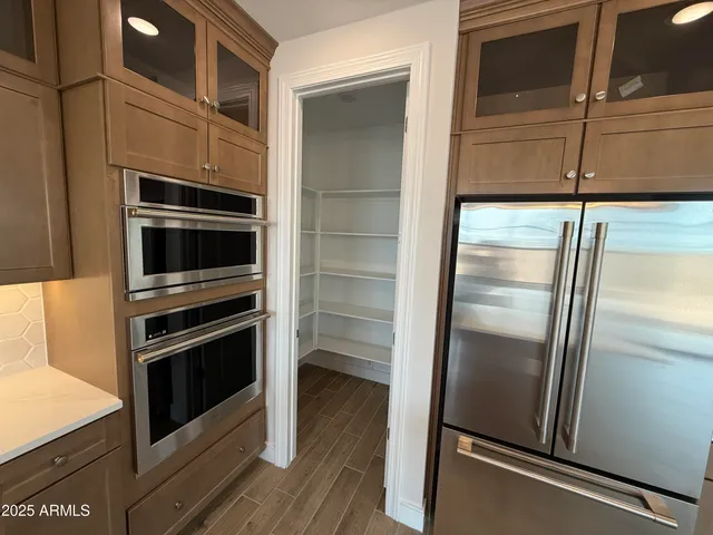 a kitchen with stainless steel appliances a sink dishwasher a refrigerator and a large mirror with wooden floor