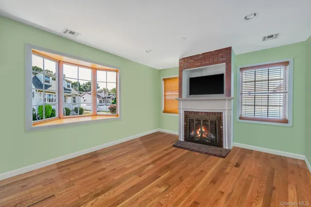 a view of an empty room with wooden floor fireplace and a window