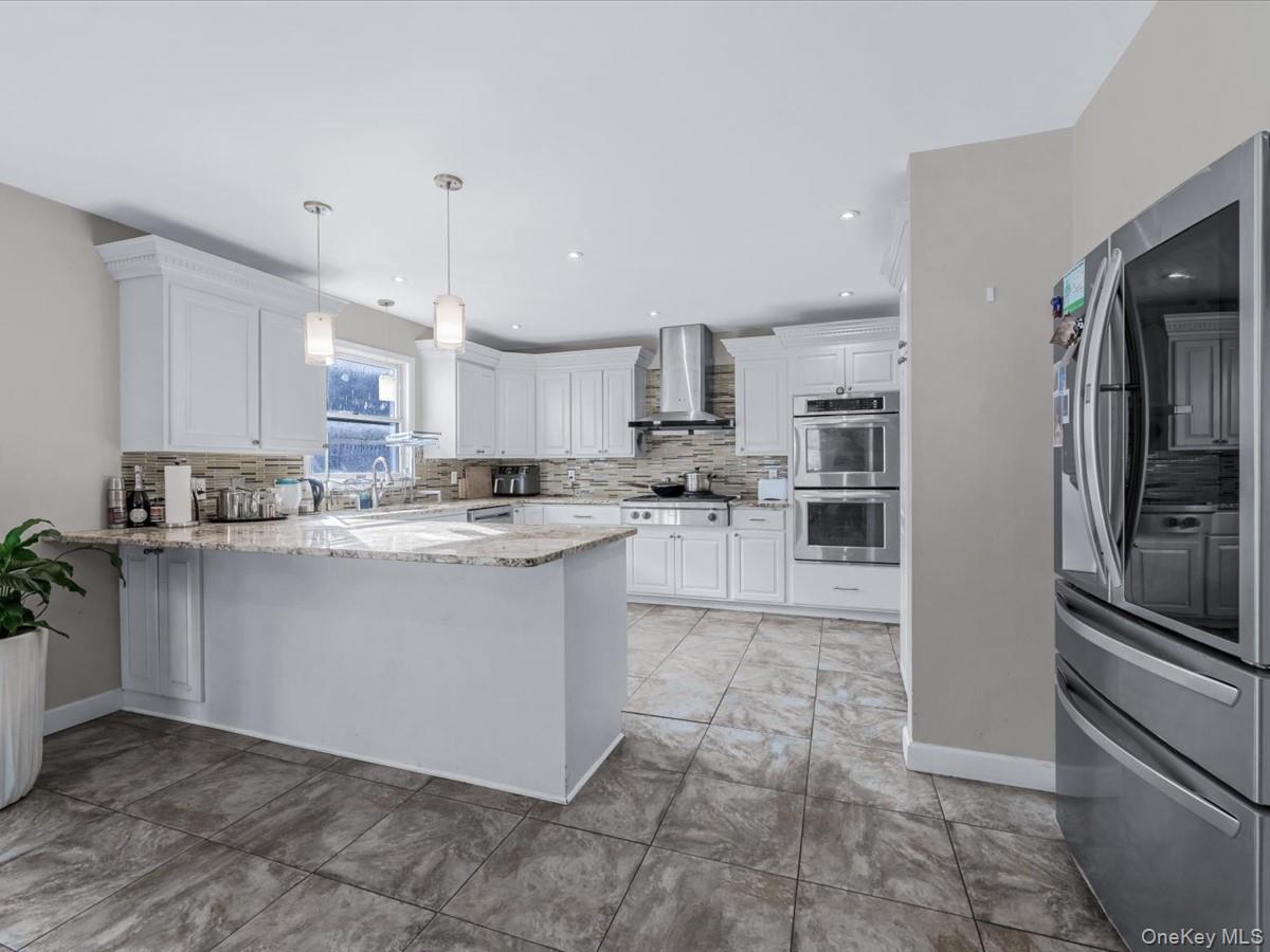 217-32 Corbett Road Queens, NY 11361 - Photo 7 of 25 Kitchen with appliances with stainless steel finishes, light stone countertops, pendant lighting, white cabinetry, and a peninsula