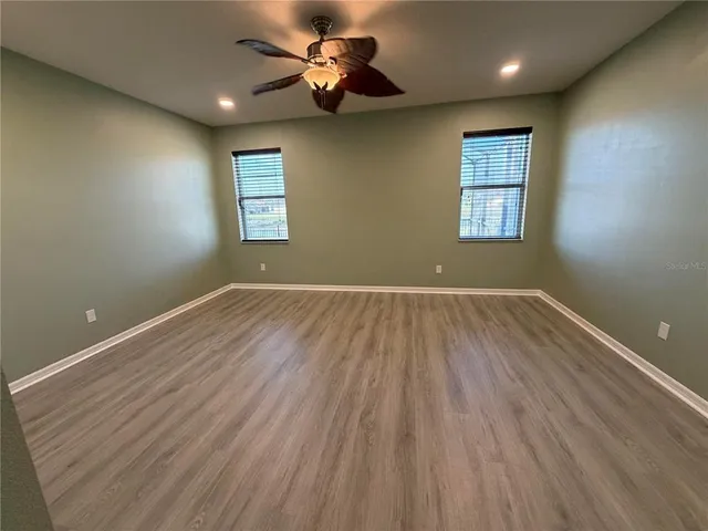 an empty room with wooden floor chandelier fan and windows