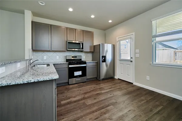 a kitchen with stainless steel appliances granite countertop a refrigerator a sink a stove a microwave and island with wooden floor