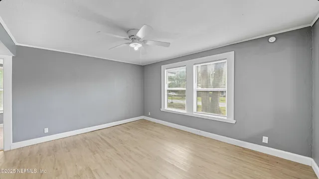an empty room with wooden floor fan and windows