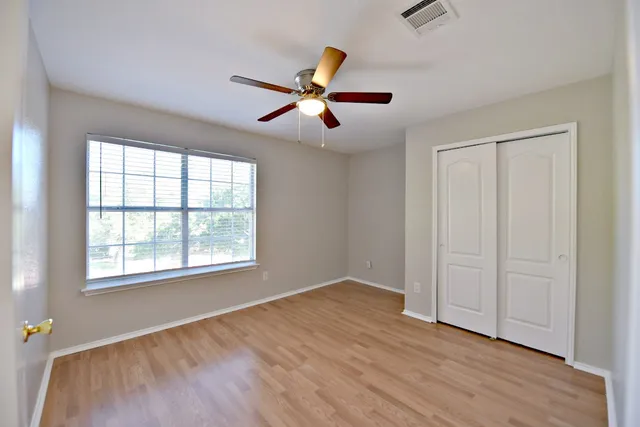 an empty room with wooden floor ceiling fan and windows