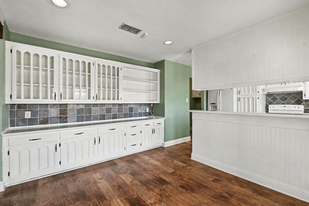 332 Cook Road Willow Park, TX 76087 - Photo 8 of 26 Expansive white built-in cabinetry with glass-front uppers and dark hardware, tile backsplash, wood-finish flooring, and a beadboard-paneled half wall