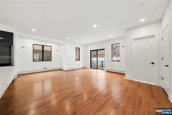 a view of empty room with wooden floor and kitchen