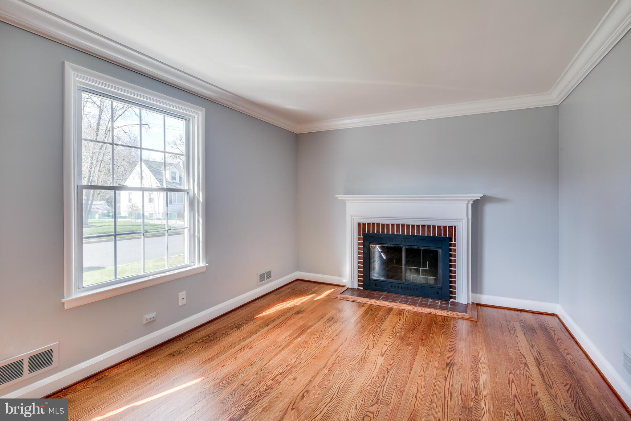 6704 Campfield Road Baltimore, MD 21207 - Photo 11 of 30 an empty room with wooden floor fireplace and windows