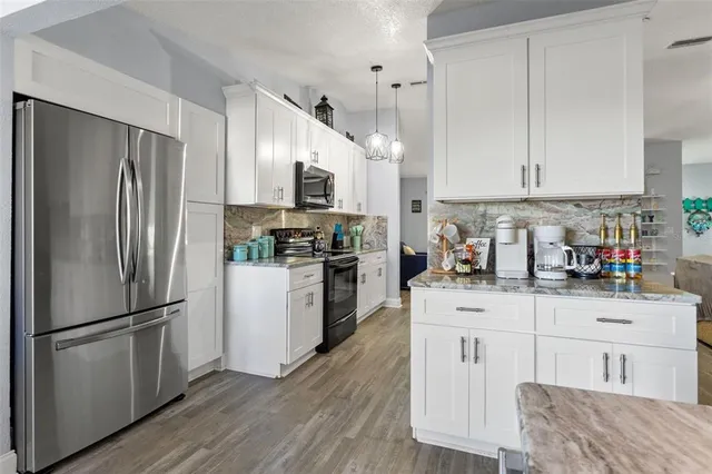 a kitchen with stainless steel appliances granite countertop a refrigerator a stove a sink a dining table and chairs with wooden floor