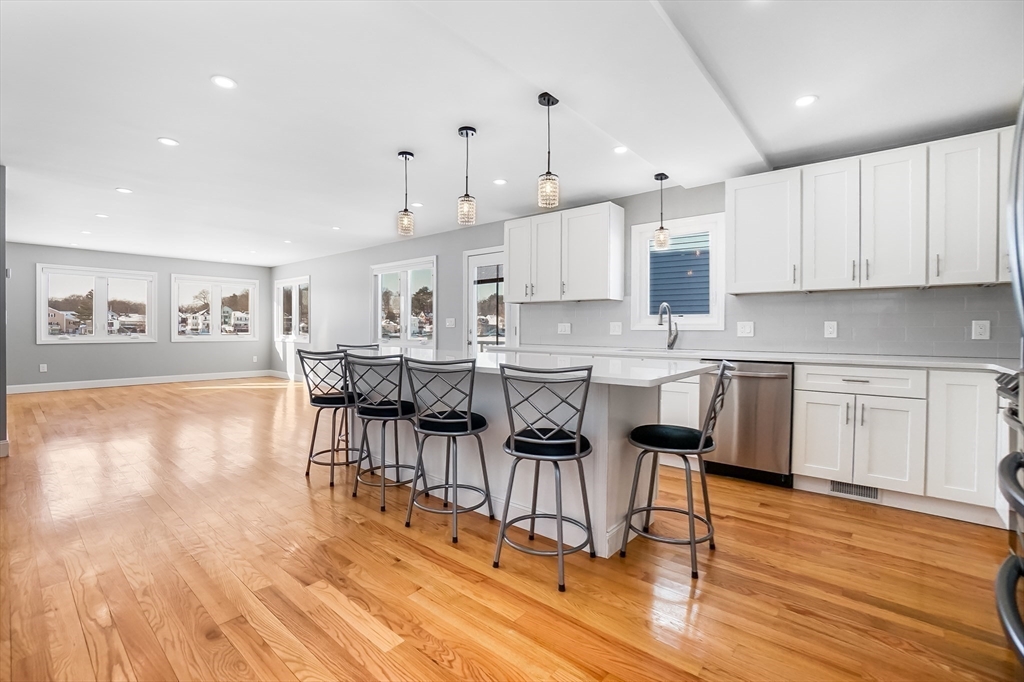52 Savory Street, Unit 52 Lynn, MA 01904 - Photo 2 of 29 a open kitchen with stainless steel appliances granite countertop a stove a refrigerator a sink a dining table and chairs with wooden floor