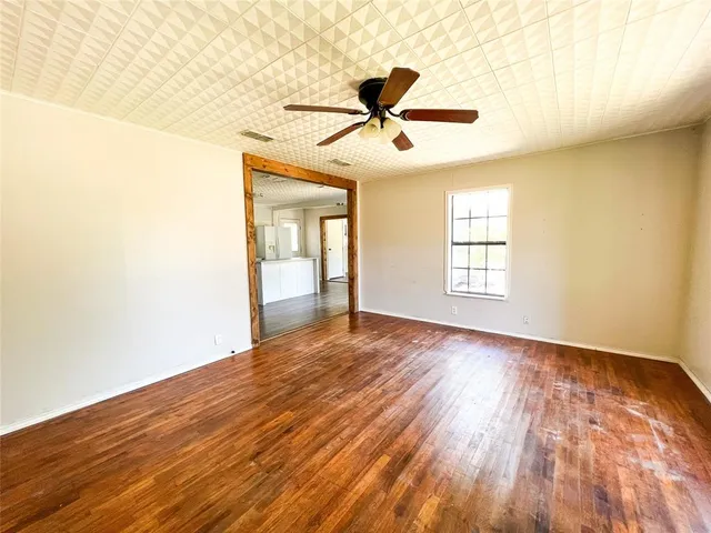 an empty room with wooden floor fan and windows