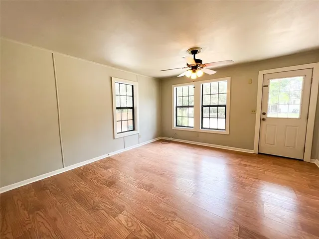 an empty room with wooden floor chandelier fan and windows