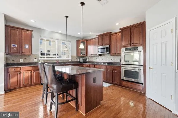 a kitchen with kitchen island granite countertop wooden floors appliances and cabinets