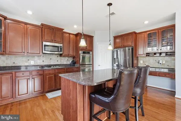 a kitchen with stainless steel appliances granite countertop a stove top oven a refrigerator a sink and a wooden cabinets