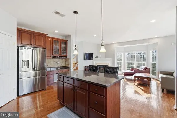 a kitchen with stainless steel appliances granite countertop a refrigerator a sink dishwasher a oven and a dining table with wooden floor
