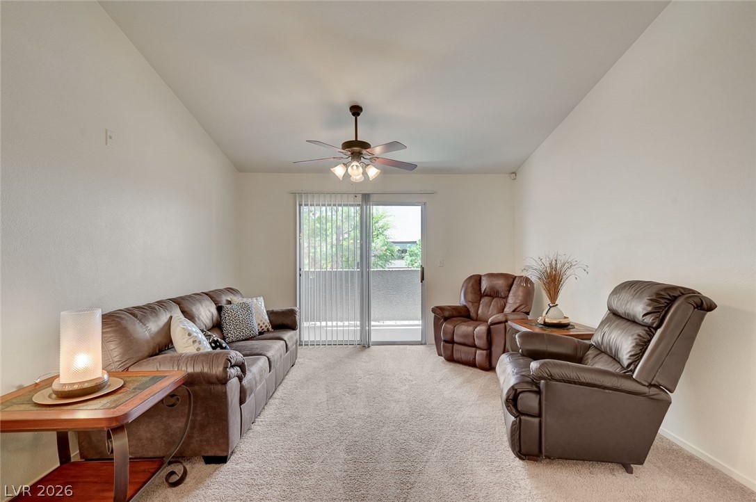 555 East Silverado Ranch Boulevard, Unit 2124 Las Vegas, NV 89183 - Photo 10 of 47 A comfortable living space boasts a ceiling fan, plush carpeting, and access to a balcony through sliding glass doors.