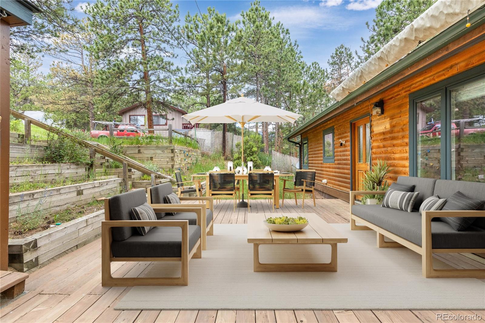 29723 Spruce Road Evergreen, CO 80439 - Photo 2 of 42 a view of a patio with couches table and chairs under an umbrella with large trees