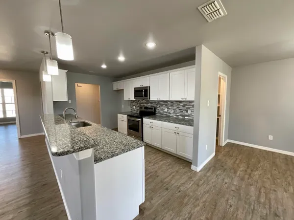 a kitchen with stainless steel appliances kitchen island granite countertop a stove top oven a sink a refrigerator white cabinets and wooden floor