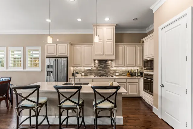 a kitchen with stainless steel appliances kitchen island granite countertop a dining table chairs stove refrigerator and cabinets