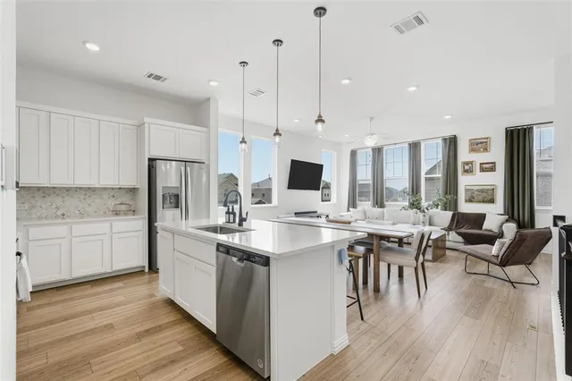 a open kitchen with stainless steel appliances granite countertop a stove top oven a refrigerator a sink and white cabinets with wooden floor