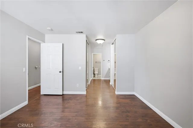 a view of an empty room with wooden floor and a bathroom