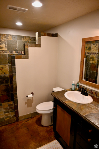 314 Brown Farm Lane Draper, UT 84020 - Photo 32 of 57 Bathroom featuring a tile vanity with an integrated sink and dark cabinet, stone tile shower, and a white commode