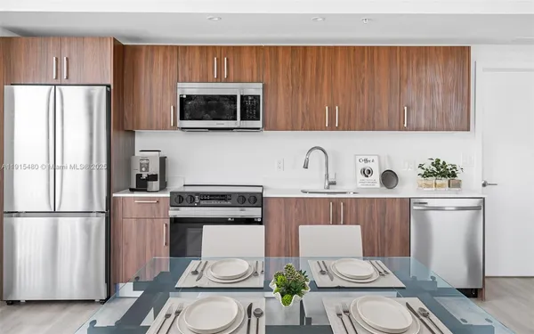 a kitchen with stainless steel appliances a stove a sink a refrigerator a microwave a dining table and chairs