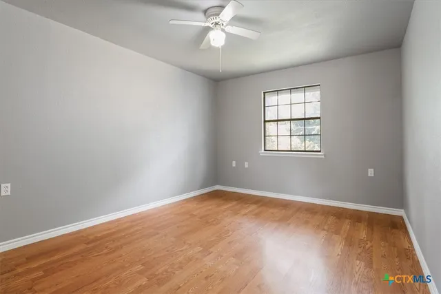 an empty room with wooden floor fan and windows