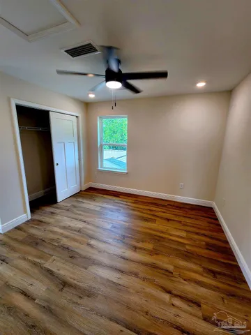 an empty room with wooden floor ceiling fan and windows
