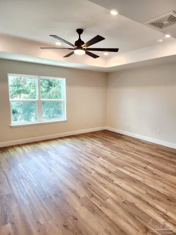 an empty room with wooden floor fan and windows