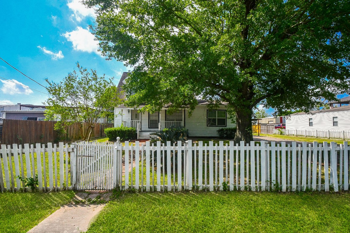 Charming home with a cozy front porch, nestled behind a white picket fence. The yard is spacious with lush greenery and a large shade tree, offering a welcoming and serene atmosphere.
