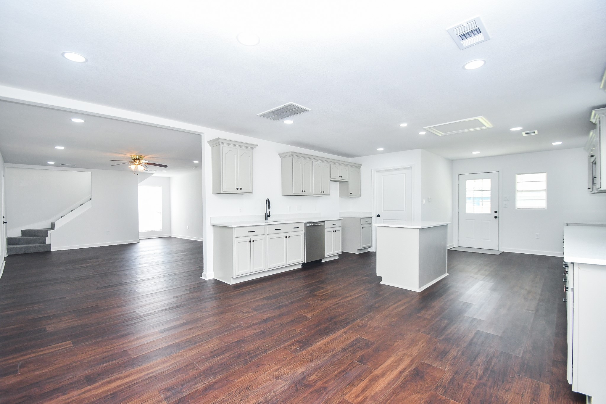 2636 Lone Oak Road Houston, TX 77093 - Photo 5 of 42 This open-concept kitchen and living area features modern white cabinetry, dark hardwood floors, and recessed lighting. A ceiling fan and large window enhance the spacious living room, while a staircase leads to the upper level.