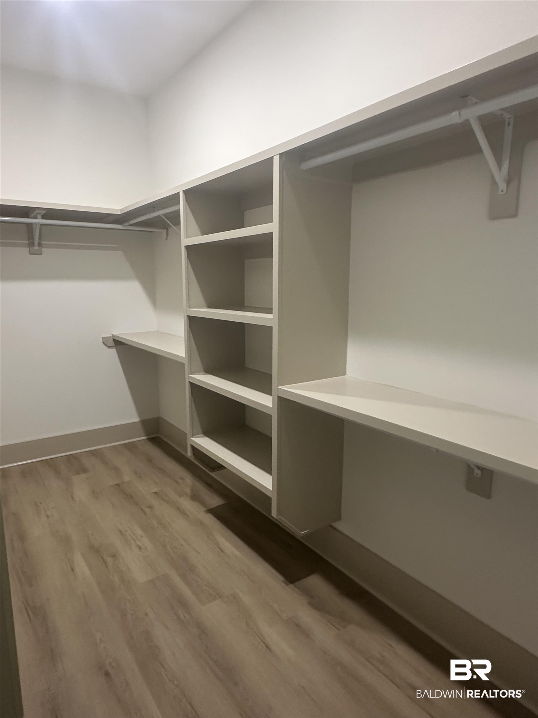 13111 Gopher Court Elberta, AL 36530 - Photo 24 of 41 Walk-in closet featuring extensive built-in shelving, multiple hanging rods, and wood-finish flooring