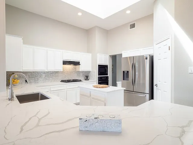 a kitchen with granite countertop a refrigerator sink and white cabinets