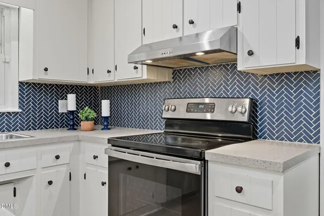 a kitchen with granite countertop a stove a sink and white cabinets