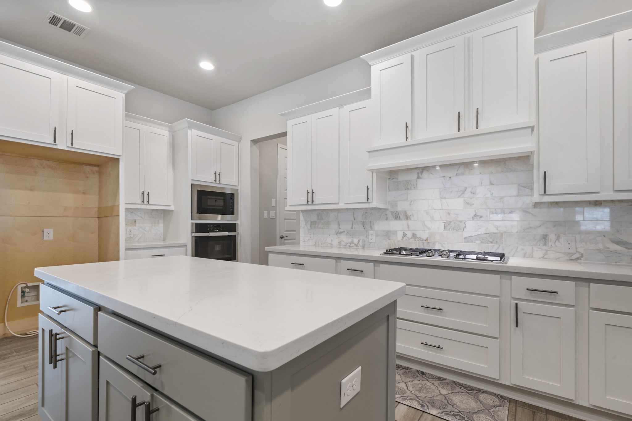 104 Catani Loop Georgetown, TX 78628 - Photo 5 of 34 The kitchen features white cabinetry with dark hardware, a spacious island with a light-colored countertop, and a gas cooktop set against a marble-patterned backsplash