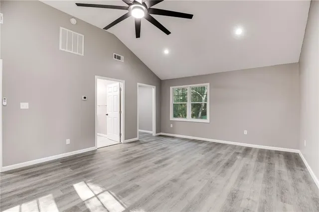 an empty room with wooden floor fan and windows